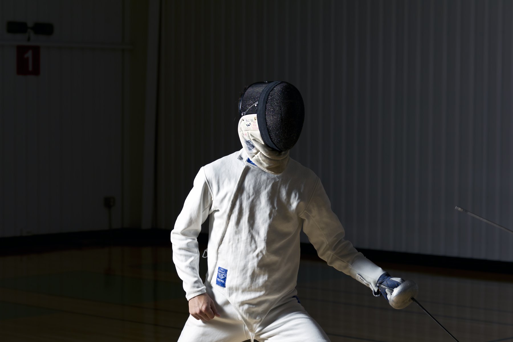 Two fencers on the strip at Woodlands Fencing Academy, national flags along the wall
